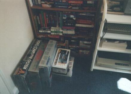 [Photo: Main games shelf with some consoles on the floor]